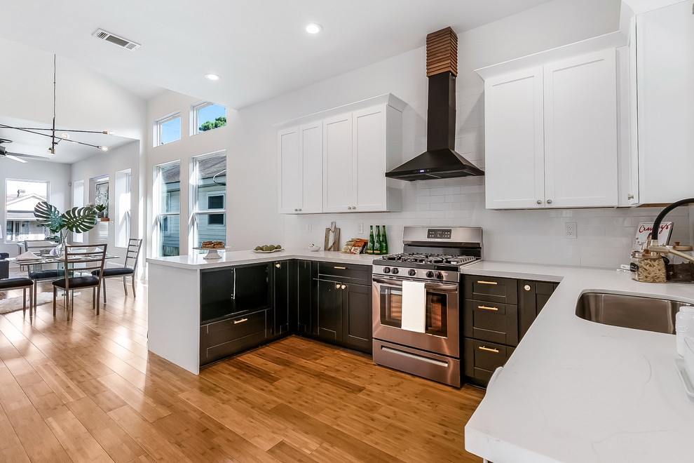 Photo of a mid-sized midcentury u-shaped open plan kitchen in New Orleans with an undermount sink, shaker cabinets, white cabinets, solid surface benchtops, white splashback, subway tile splashback, stainless steel appliances, bamboo floors, no island, brown floor and white benchtop.