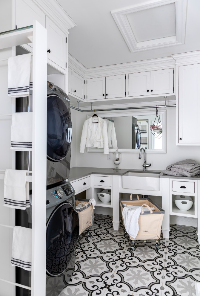 Small transitional l-shaped dedicated laundry room in Other with a farmhouse sink, white cabinets, quartz benchtops, white walls, porcelain floors, a stacked washer and dryer, grey benchtop, beaded inset cabinets and multi-coloured floor.