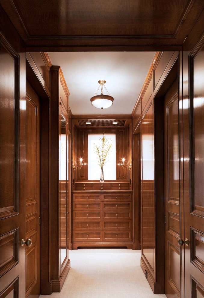 Large traditional gender-neutral walk-in wardrobe in New York with recessed-panel cabinets, dark wood cabinets and carpet.