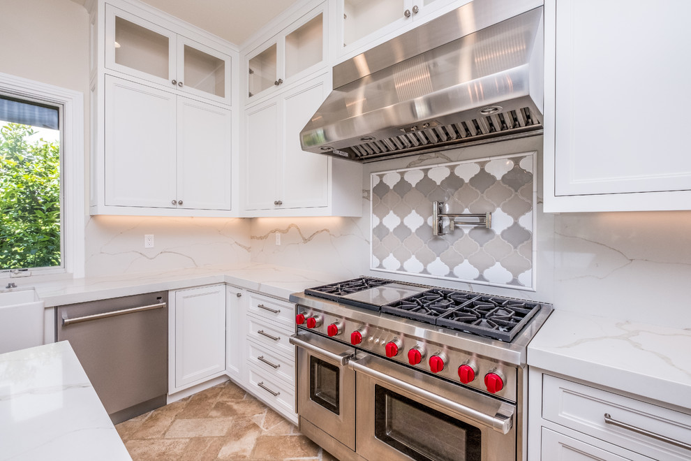 Mid-sized transitional l-shaped porcelain tile and beige floor enclosed kitchen photo in Orange County with recessed-panel cabinets, white cabinets, quartz countertops, white backsplash, marble backsplash, stainless steel appliances, an island and a farmhouse sink