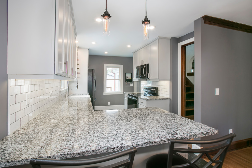This is an example of a transitional galley separate kitchen in Minneapolis with a farmhouse sink, shaker cabinets, white cabinets, granite benchtops, white splashback, subway tile splashback, black appliances, ceramic floors, no island and grey floor.