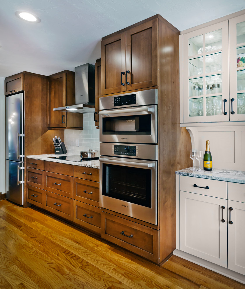 Design ideas for a mid-sized traditional galley separate kitchen in Minneapolis with an undermount sink, recessed-panel cabinets, medium wood cabinets, quartz benchtops, white splashback, subway tile splashback, stainless steel appliances, medium hardwood floors, no island and brown floor.