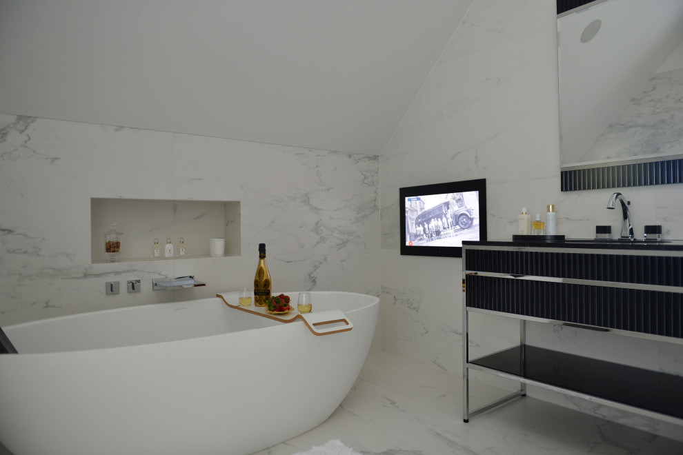 Inspiration for an expansive contemporary master bathroom in London with furniture-like cabinets, black cabinets, a freestanding tub, a shower/bathtub combo, a wall-mount toilet, white tile, marble, white walls, marble floors, a drop-in sink, solid surface benchtops, white floor, an open shower and black benchtops.