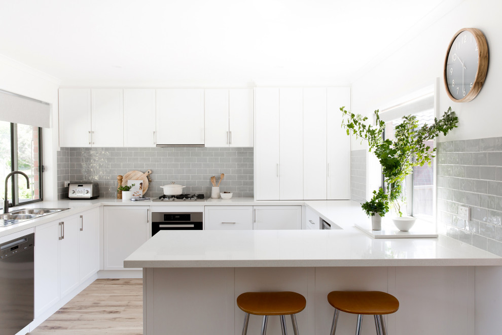 Example of a mid-sized trendy u-shaped vinyl floor eat-in kitchen design in Other with a double-bowl sink, shaker cabinets, white cabinets, quartz countertops, gray backsplash, subway tile backsplash, stainless steel appliances, a peninsula and white countertops