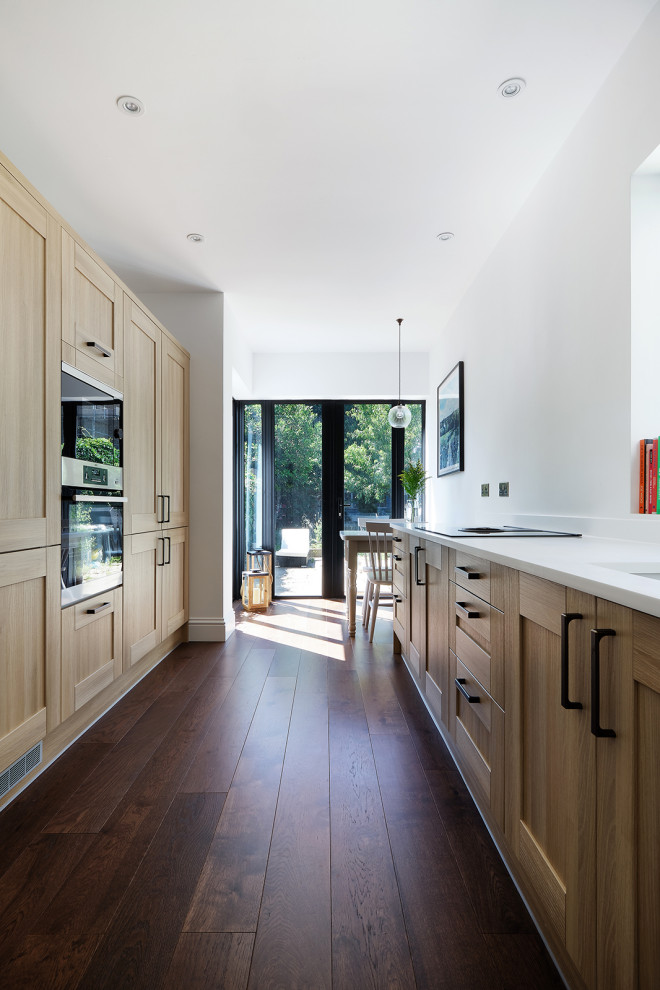 Design ideas for a mid-sized contemporary galley eat-in kitchen in London with a drop-in sink, shaker cabinets, light wood cabinets, solid surface benchtops, white splashback, no island and white benchtop.