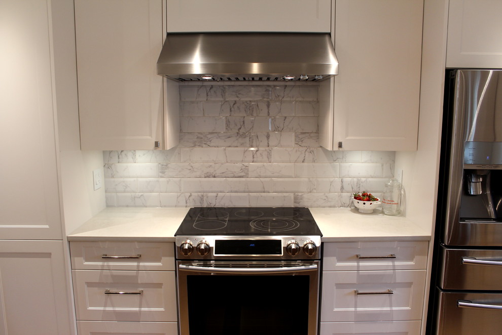 Large transitional l-shaped light wood floor eat-in kitchen photo with an undermount sink, shaker cabinets, white cabinets, quartz countertops, white backsplash, ceramic backsplash, stainless steel appliances and an island