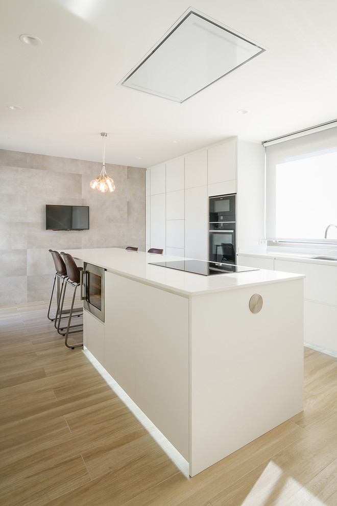 Inspiration for a contemporary galley kitchen in Madrid with flat-panel cabinets, white cabinets, quartz benchtops, black appliances, with island, white benchtop, light hardwood floors and beige floor.