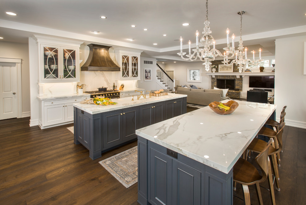 Design ideas for a large traditional galley open plan kitchen in Cincinnati with a farmhouse sink, quartz benchtops, white splashback, stone slab splashback, dark hardwood floors, multiple islands, white cabinets, black appliances and recessed-panel cabinets.
