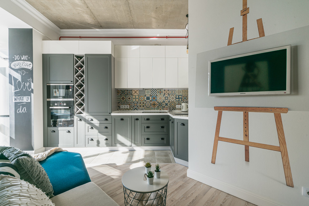Small eclectic l-shaped open plan kitchen in Moscow with an undermount sink, raised-panel cabinets, grey cabinets, solid surface benchtops, multi-coloured splashback, ceramic splashback, black appliances, porcelain floors, no island, grey floor and white benchtop.