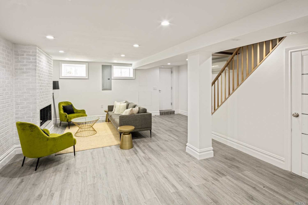 Photo of a mid-sized contemporary look-out basement in New York with white walls, vinyl floors, a standard fireplace, a brick fireplace surround, grey floor and brick walls.