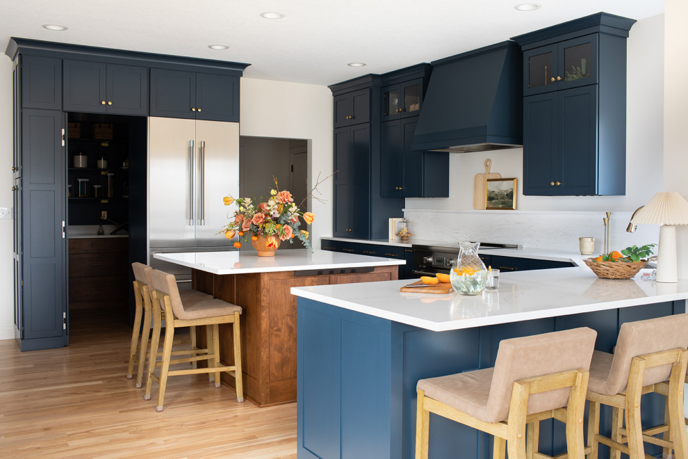 Large transitional light wood floor kitchen photo with an undermount sink, shaker cabinets, blue cabinets, quartz countertops, white backsplash, quartz backsplash, stainless steel appliances, an island and white countertops