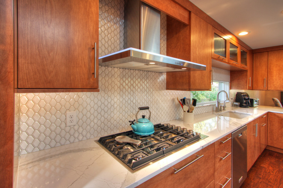 Expansive modern u-shaped open plan kitchen in St Louis with an undermount sink, flat-panel cabinets, quartz benchtops, white splashback, porcelain splashback, stainless steel appliances, medium hardwood floors and with island.