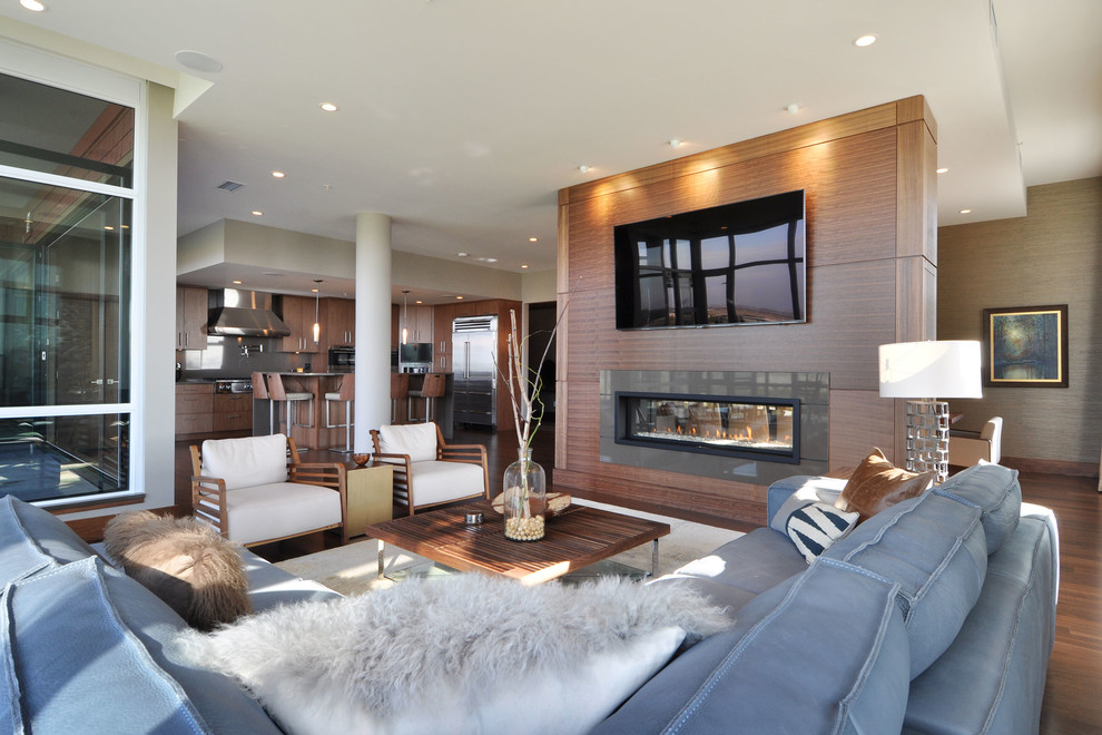 Design ideas for a mid-sized contemporary open concept living room in Vancouver with medium hardwood floors, a two-sided fireplace, a wood fireplace surround and a wall-mounted tv.