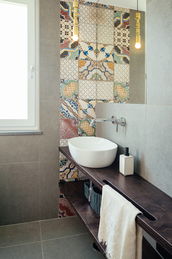 Photo of a contemporary bathroom in Naples with open cabinets, dark wood cabinets, porcelain floors, a vessel sink, wood benchtops, grey floor, brown benchtops, multi-coloured tile and cement tile.