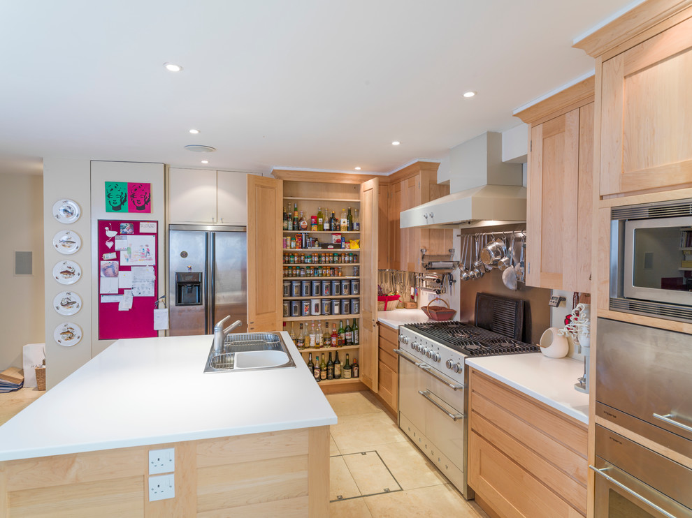 This is an example of a mid-sized galley open plan kitchen in Other with a triple-bowl sink, recessed-panel cabinets, light wood cabinets, solid surface benchtops, metallic splashback, stainless steel appliances, limestone floors and with island.