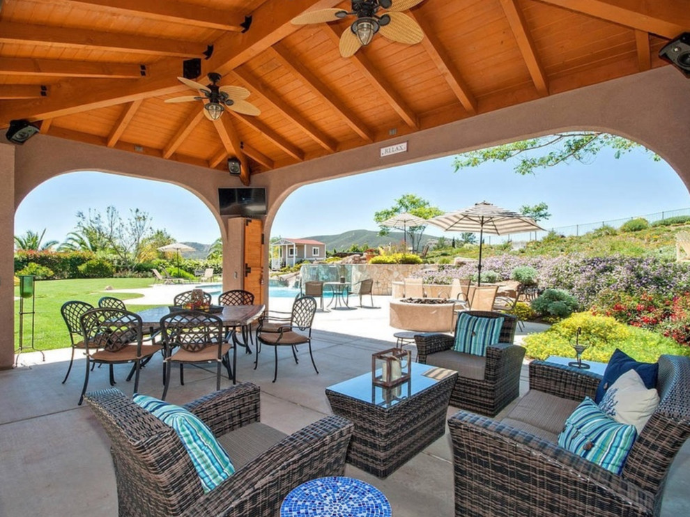 This is an example of a large beach style backyard patio in San Diego with a fire feature, concrete slab and a pergola.