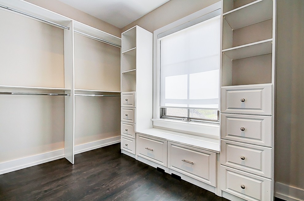 This is an example of a large traditional gender-neutral walk-in wardrobe in Toronto with raised-panel cabinets, white cabinets, dark hardwood floors and brown floor.