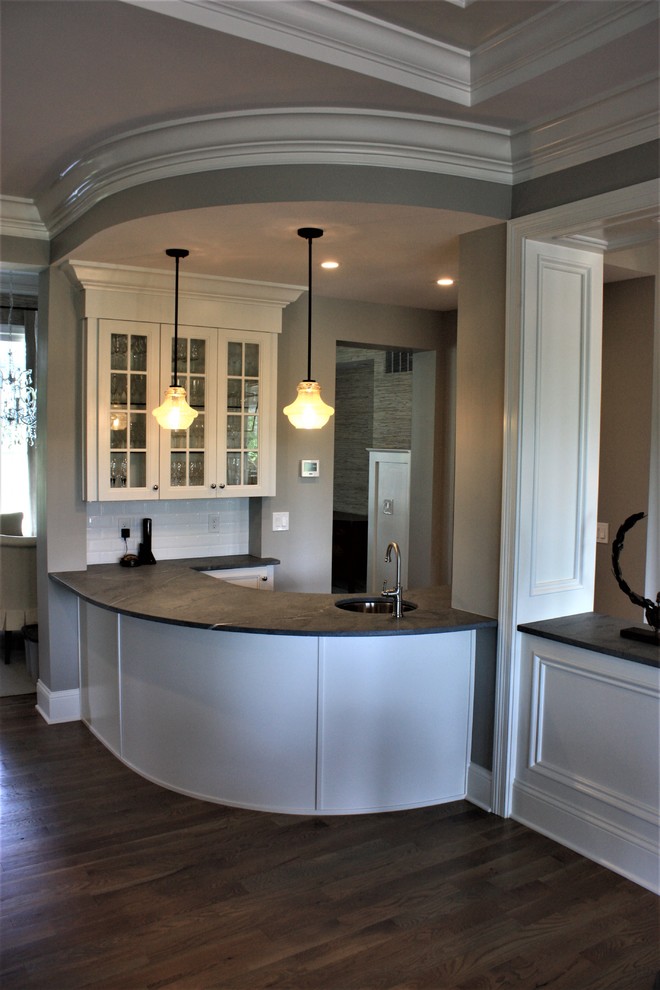 Inspiration for a transitional wet bar in Cincinnati with an undermount sink, recessed-panel cabinets, white cabinets, soapstone benchtops, white splashback, subway tile splashback, dark hardwood floors and brown floor.