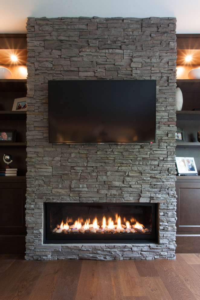 Design ideas for a large traditional family room in Vancouver with grey walls, medium hardwood floors, a ribbon fireplace, a stone fireplace surround and a wall-mounted tv.