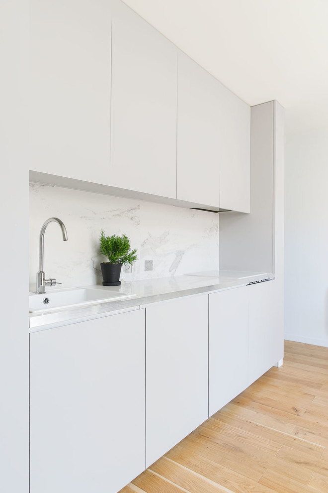 This is an example of a small contemporary single-wall open plan kitchen in Lyon with a single-bowl sink, beaded inset cabinets, grey cabinets, tile benchtops, white splashback and light hardwood floors.