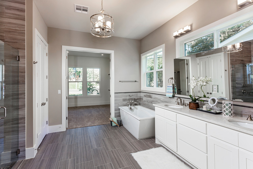 Inspiration for a mid-sized country master bathroom in Austin with recessed-panel cabinets, white cabinets, a freestanding tub, a curbless shower, a one-piece toilet, gray tile, porcelain tile, grey walls, plywood floors, an undermount sink and solid surface benchtops.