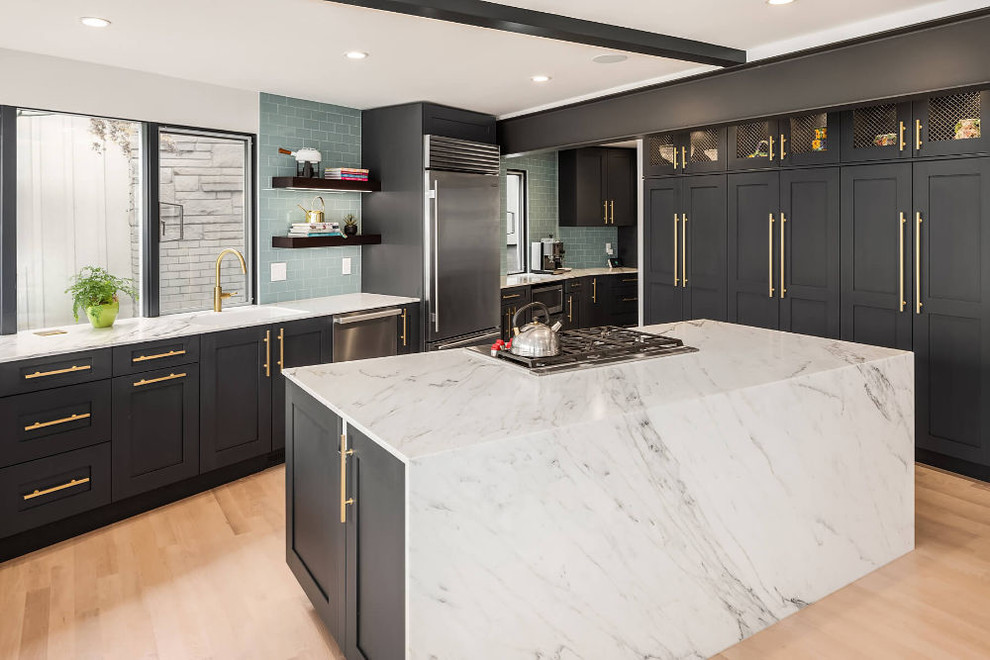 Large contemporary u-shaped eat-in kitchen in Seattle with an undermount sink, recessed-panel cabinets, black cabinets, marble benchtops, green splashback, glass tile splashback, stainless steel appliances, light hardwood floors, with island, brown floor and white benchtop.