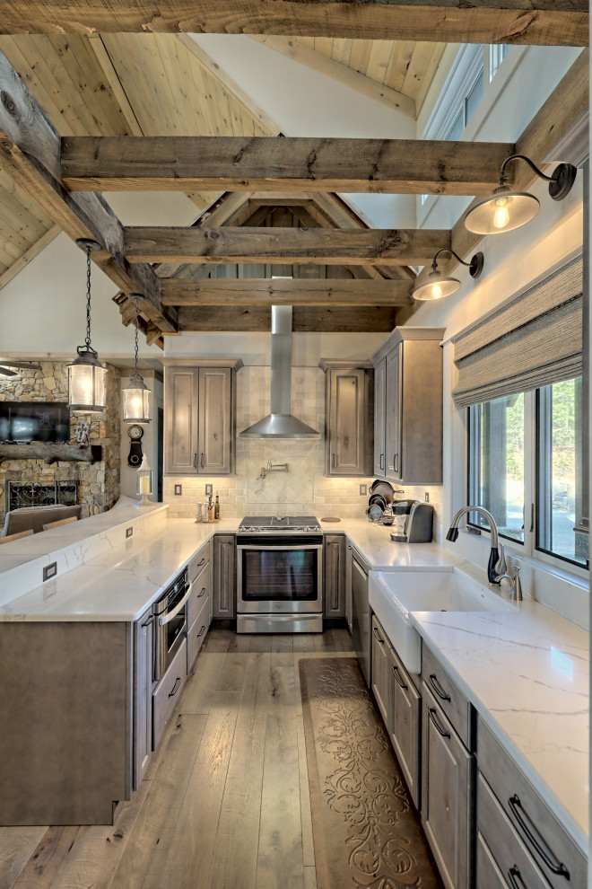 Photo of a small country u-shaped open plan kitchen in Atlanta with a farmhouse sink, raised-panel cabinets, light wood cabinets, quartz benchtops, white splashback, travertine splashback, stainless steel appliances, a peninsula, brown floor and white benchtop.