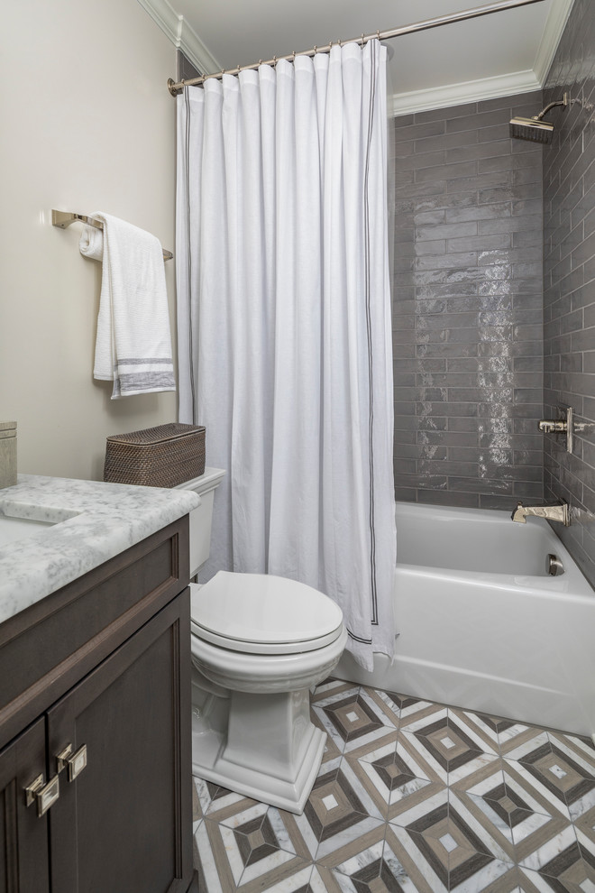 Photo of a small transitional kids bathroom in Charlotte with dark wood cabinets, an alcove tub, a shower/bathtub combo, a two-piece toilet, gray tile, ceramic tile, grey walls, an undermount sink, marble benchtops, multi-coloured floor, a shower curtain, white benchtops and recessed-panel cabinets.