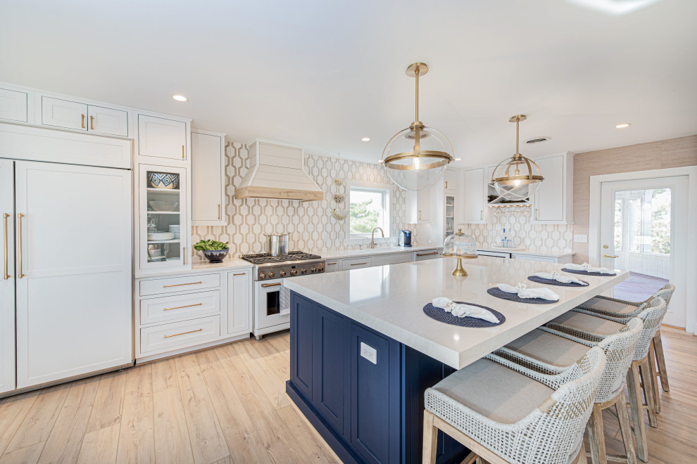 Inspiration for a large beach style single-wall kitchen in Other with an undermount sink, beaded inset cabinets, white cabinets, quartz benchtops, white splashback, marble splashback, white appliances, vinyl floors, with island, beige floor and beige benchtop.