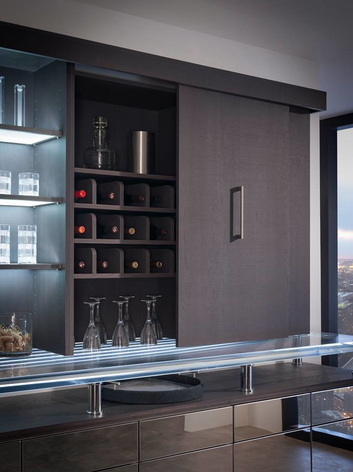 This is an example of a mid-sized modern single-wall seated home bar in Houston with flat-panel cabinets, dark wood cabinets, glass benchtops, brown splashback and vinyl floors.