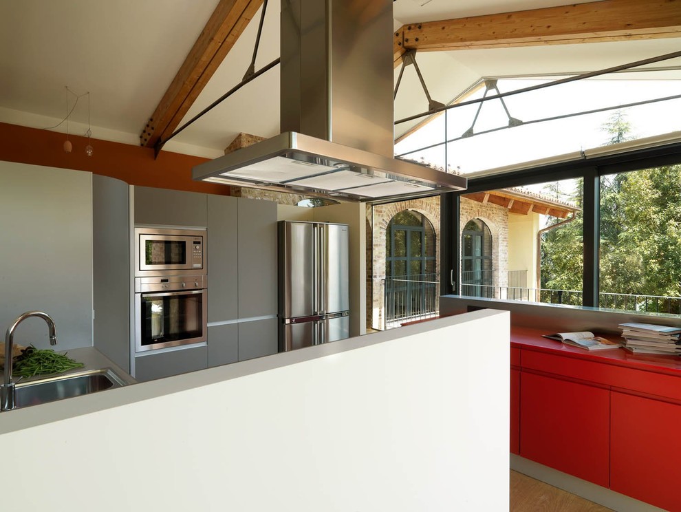This is an example of an expansive contemporary u-shaped open plan kitchen in Turin with a double-bowl sink, flat-panel cabinets, red cabinets, solid surface benchtops, grey splashback, stainless steel appliances, medium hardwood floors and multiple islands.