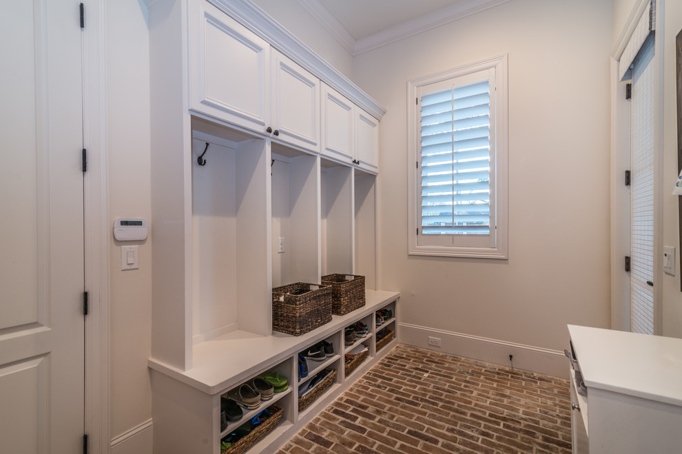 This is an example of a mid-sized country gender-neutral walk-in wardrobe with white cabinets and brick floors.