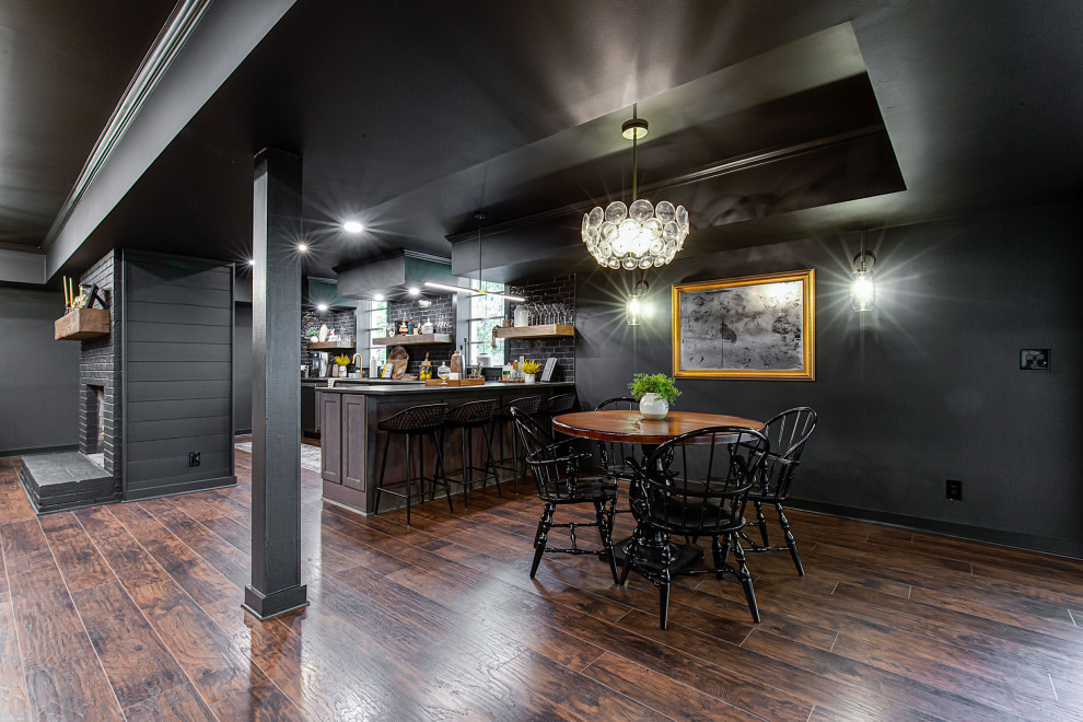 Modern inredning av en stor källare ovan mark, med en hemmabar, svarta väggar, vinylgolv, en standard öppen spis, en spiselkrans i tegelsten och brunt golv