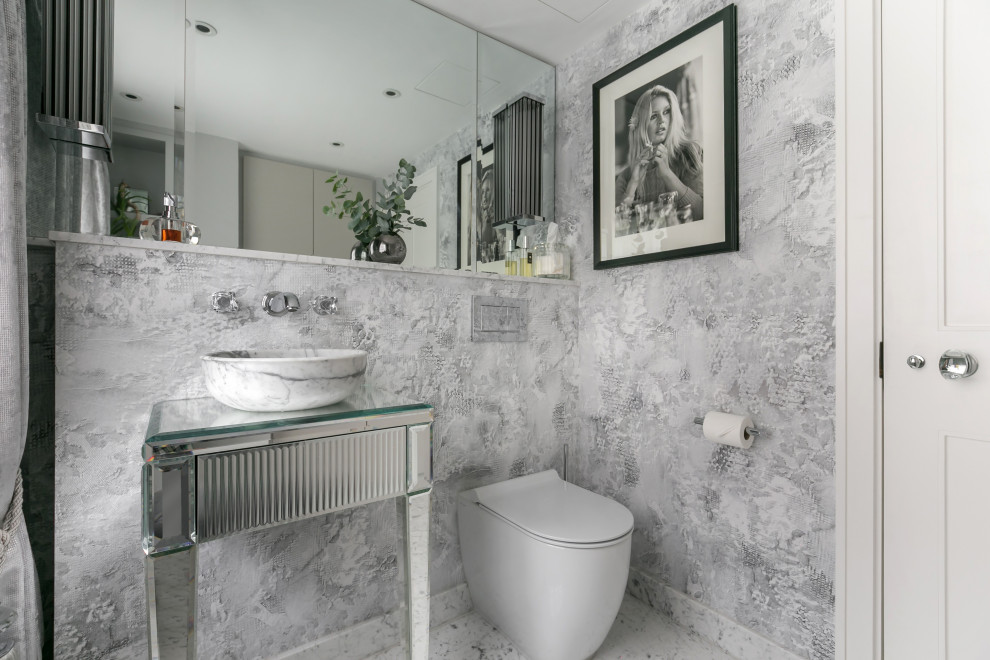 ロンドンにあるラグジュアリーな中くらいなトランジショナルスタイルのおしゃれなトイレ・洗面所 (ガラス扉のキャビネット、一体型トイレ	、グレーの壁、大理石の床、ベッセル式洗面器、ガラスの洗面台、白い床、独立型洗面台、壁紙) の写真