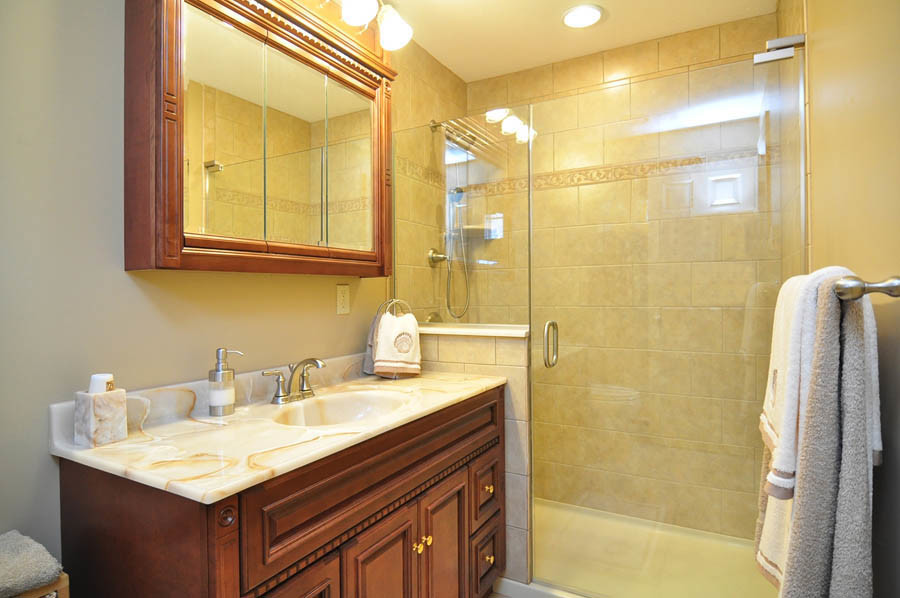 Small traditional bathroom in Charlotte with brown cabinets, a two-piece toilet, beige tile, ceramic tile, beige walls, ceramic floors, an integrated sink, onyx benchtops, beige floor and a hinged shower door.