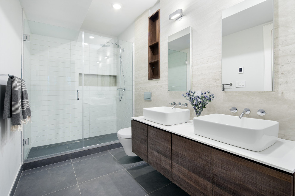 Mid-sized trendy master white tile and travertine tile porcelain tile, gray floor and double-sink alcove shower photo in New York with flat-panel cabinets, dark wood cabinets, a wall-mount toilet, white walls, a vessel sink, quartz countertops, a hinged shower door, white countertops, a floating vanity and a niche