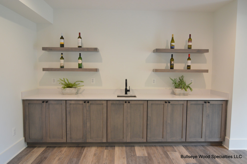 Photo of a medium sized traditional single-wall wet bar in DC Metro with a submerged sink, shaker cabinets, grey cabinets, engineered stone countertops, laminate floors, brown floors and white worktops.