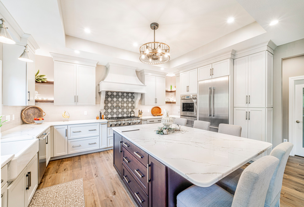 Open concept kitchen - large transitional u-shaped medium tone wood floor, gray floor and tray ceiling open concept kitchen idea with a farmhouse sink, shaker cabinets, white cabinets, granite countertops, multicolored backsplash, ceramic backsplash, stainless steel appliances, an island and white countertops