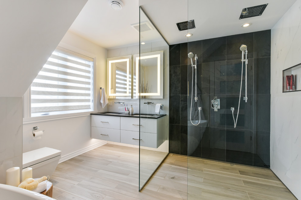 Inspiration for a mid-sized contemporary master bathroom in Montreal with flat-panel cabinets, white cabinets, a freestanding tub, a curbless shower, white walls, an undermount sink, solid surface benchtops, a one-piece toilet, black tile and an open shower.