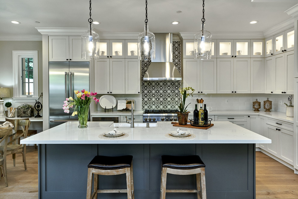 Inspiration for a mid-sized mediterranean l-shaped eat-in kitchen in San Francisco with a farmhouse sink, shaker cabinets, white cabinets, quartz benchtops, stainless steel appliances, with island, white benchtop, multi-coloured splashback, light hardwood floors and beige floor.