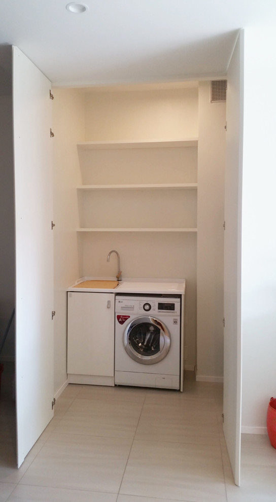This is an example of a small contemporary l-shaped dedicated laundry room in Milan with an utility sink, flat-panel cabinets, white cabinets, solid surface benchtops, white walls, porcelain floors and beige floor.