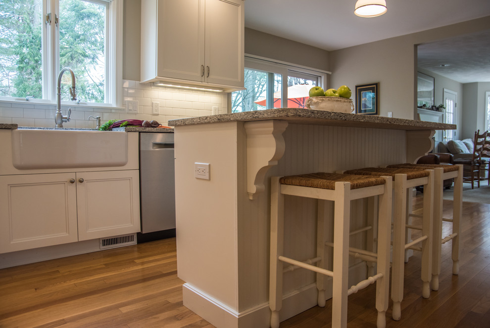 Eat-in kitchen - mid-sized transitional l-shaped medium tone wood floor eat-in kitchen idea in Boston with a farmhouse sink, shaker cabinets, white cabinets, quartz countertops, white backsplash, subway tile backsplash, stainless steel appliances and an island