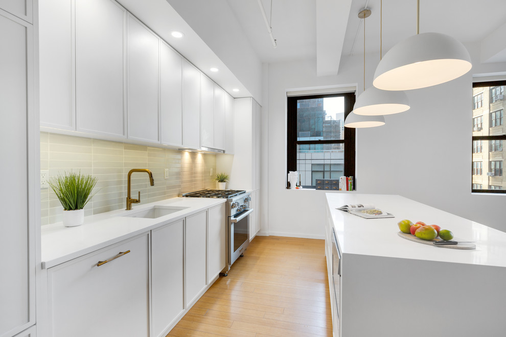 Inspiration for a transitional kitchen in New York with an undermount sink, shaker cabinets, white cabinets, quartz benchtops, green splashback, panelled appliances, light hardwood floors and white benchtop.