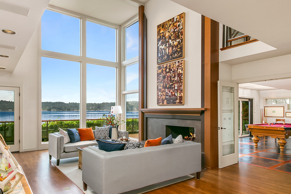 Inspiration for a large transitional open concept living room in Seattle with white walls, medium hardwood floors, a concrete fireplace surround and a two-sided fireplace.