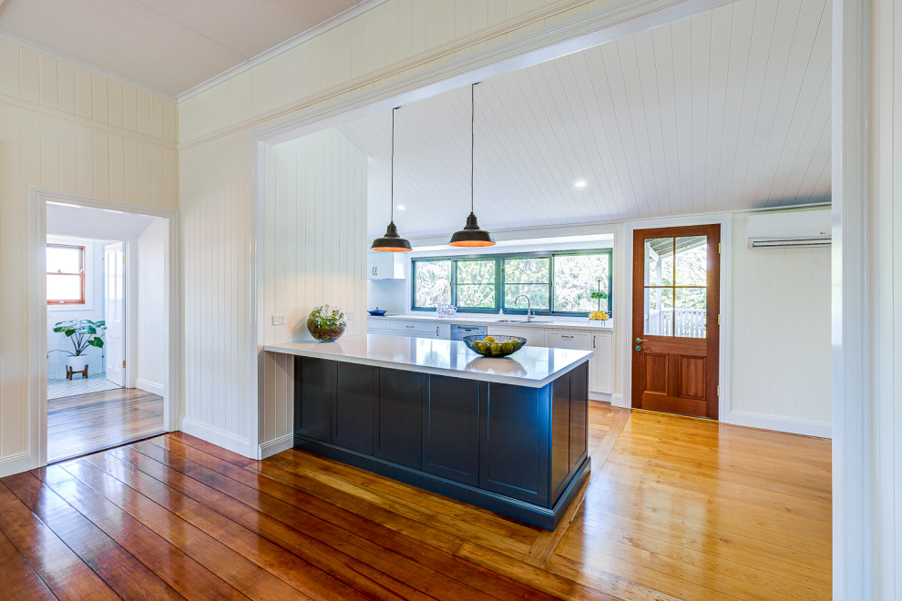 Expansive contemporary galley kitchen/diner in Brisbane with a double-bowl sink, shaker cabinets, white cabinets, engineered stone countertops, white splashback, engineered quartz splashback, stainless steel appliances, light hardwood flooring, an island, brown floors, white worktops and a wood ceiling.