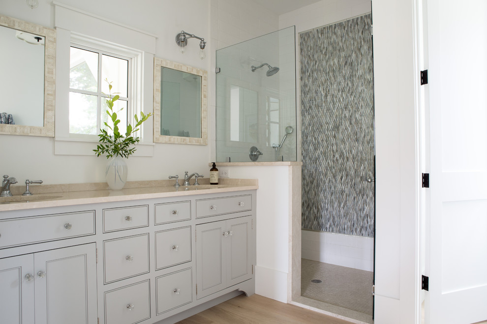 Mid-sized beach style master bathroom in Charleston with beaded inset cabinets, grey cabinets, mosaic tile, white walls, light hardwood floors, an undermount sink, beige floor, beige benchtops, white tile and limestone benchtops.