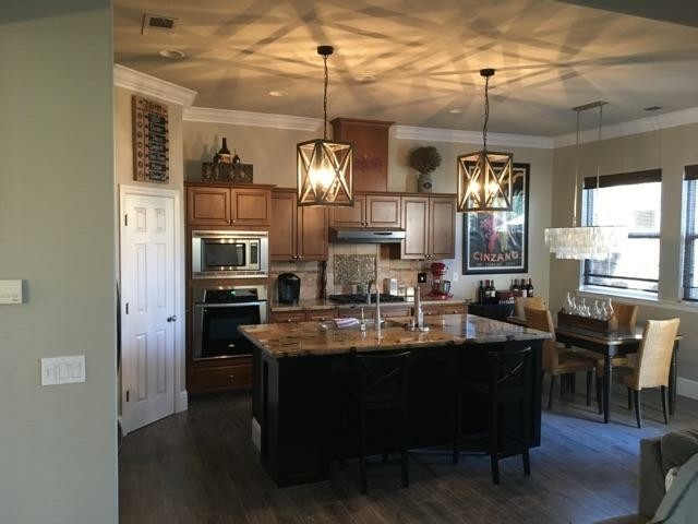 Inspiration for a small transitional galley laminate floor and brown floor open concept kitchen remodel with an undermount sink, raised-panel cabinets, medium tone wood cabinets, granite countertops, beige backsplash, stone tile backsplash, stainless steel appliances and an island
