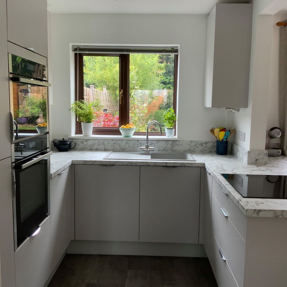 This is an example of a small contemporary u-shaped eat-in kitchen in Buckinghamshire with flat-panel cabinets, grey cabinets, laminate benchtops, panelled appliances, a peninsula and grey benchtop.