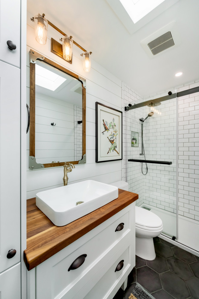 Inspiration for a mid-sized transitional 3/4 bathroom in Other with shaker cabinets, white cabinets, an alcove shower, a two-piece toilet, white tile, subway tile, white walls, a vessel sink, wood benchtops, black floor, a sliding shower screen and brown benchtops.