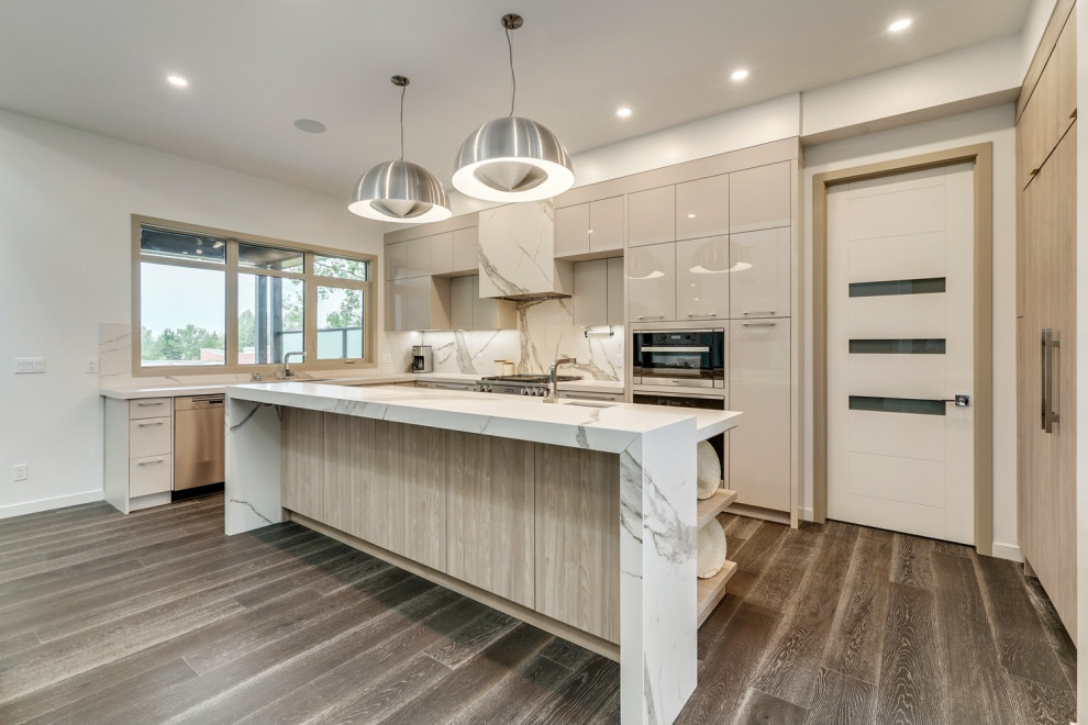 This is an example of a contemporary l-shaped kitchen in Calgary with flat-panel cabinets, beige cabinets, white splashback, stone slab splashback, dark hardwood floors, with island, brown floor and white benchtop.